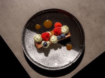 A visually appealing dessert plate with colorful garnishes including raspberries and blueberries, artistically arranged with a light dusting of powdered sugar.