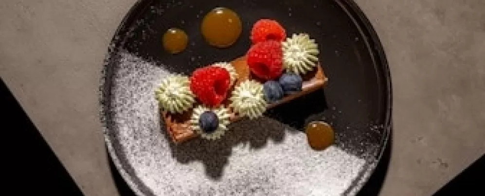A visually appealing dessert plate with colorful garnishes including raspberries and blueberries, artistically arranged with a light dusting of powdered sugar.